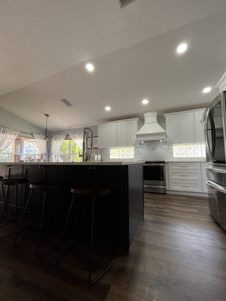 Remodeled kitchen with a black island, white cabinets and a white range hood, Tampa Bay